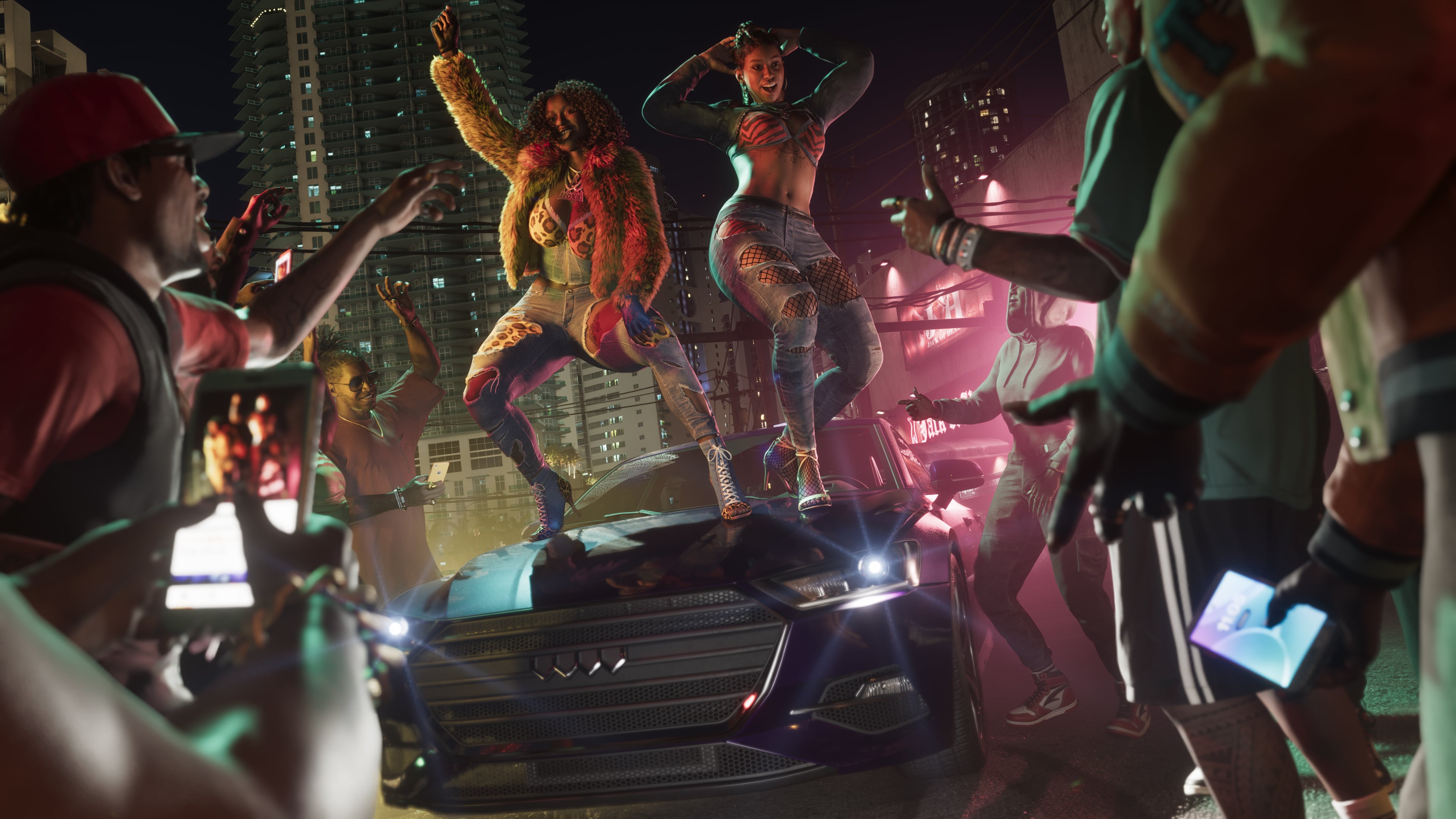 Nighttime street party with dancers on car and crowd filming with phones in neon-lit urban environment
